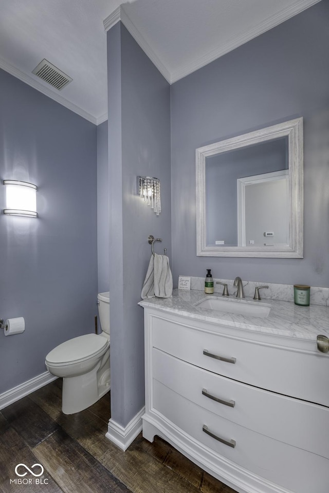 bathroom with toilet, wood finished floors, baseboards, visible vents, and ornamental molding