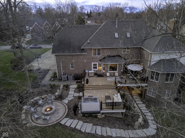 back of property with a wooden deck, brick siding, an outdoor living space with a fire pit, a shingled roof, and central AC unit