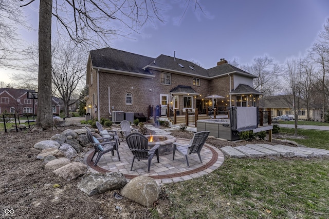 back of house featuring a wooden deck, a patio, a chimney, brick siding, and a fire pit