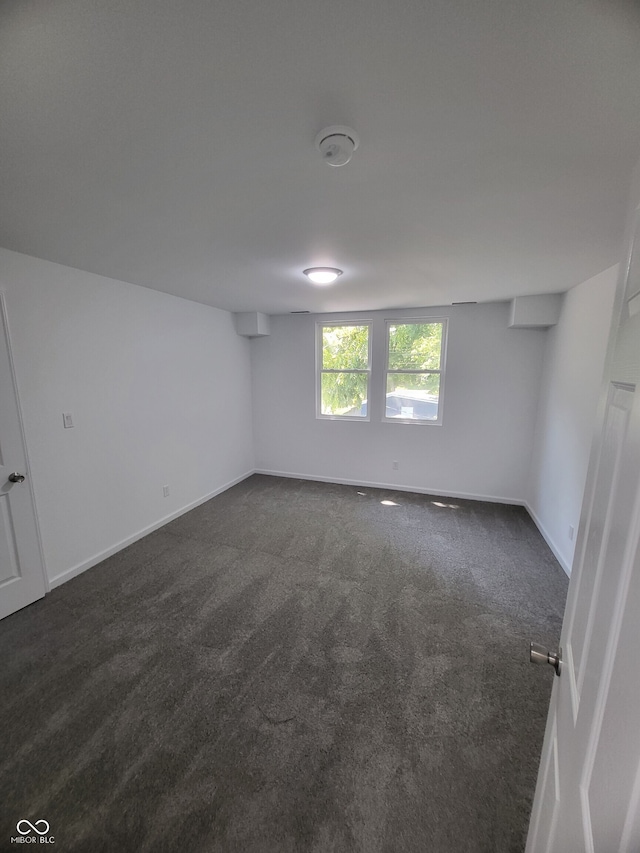 unfurnished room featuring baseboards and dark colored carpet
