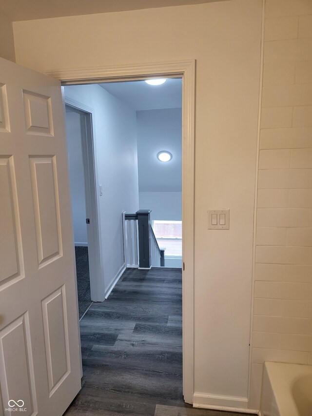 hall featuring an upstairs landing, dark wood-type flooring, and baseboards