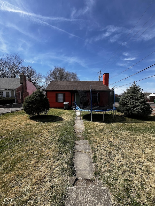 back of property with a lawn, a chimney, fence, and a trampoline