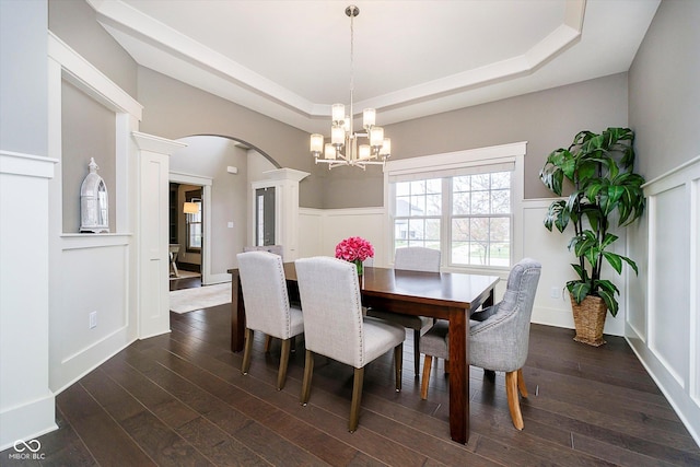 dining space with arched walkways, a notable chandelier, dark wood-style floors, and a raised ceiling