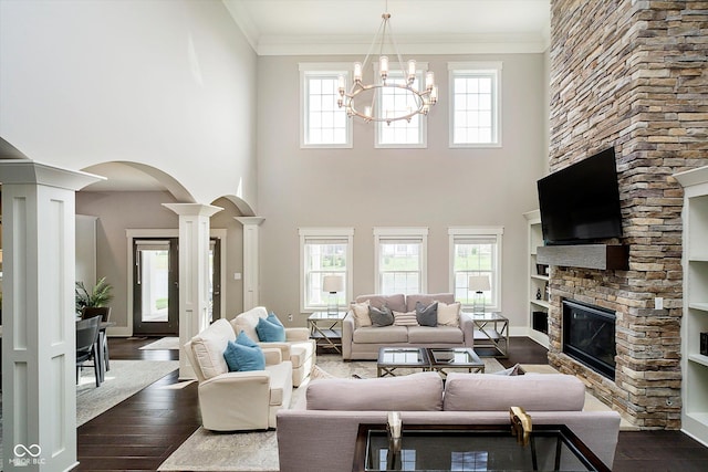 living room featuring an inviting chandelier, dark wood-type flooring, arched walkways, decorative columns, and a fireplace