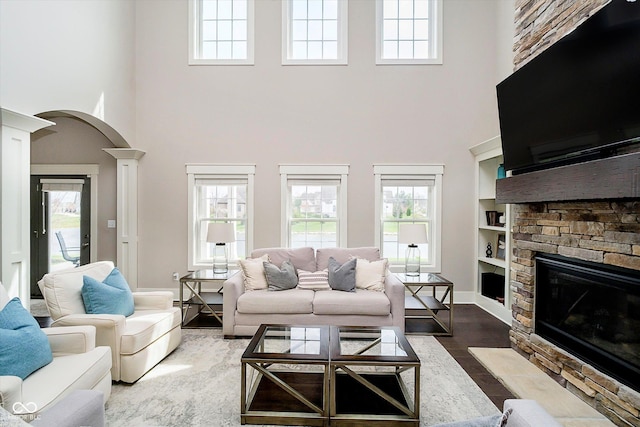 living area featuring a stone fireplace, a high ceiling, arched walkways, and a healthy amount of sunlight