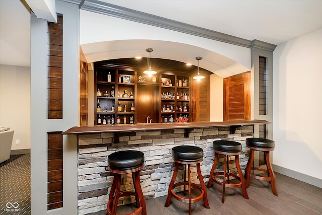 bar featuring wood finished floors, a bar, ornamental molding, baseboards, and hanging light fixtures