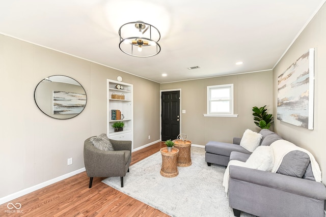 living room featuring visible vents, baseboards, ornamental molding, and wood finished floors