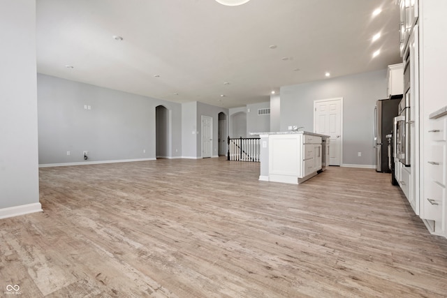 kitchen featuring light wood finished floors, arched walkways, white cabinetry, open floor plan, and freestanding refrigerator