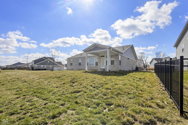 back of house featuring a lawn, fence, and brick siding