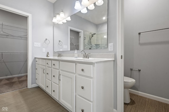 full bathroom with double vanity, a tile shower, toilet, a sink, and a walk in closet