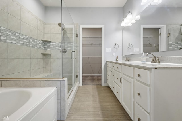 bathroom featuring a bath, a shower stall, double vanity, a sink, and a spacious closet