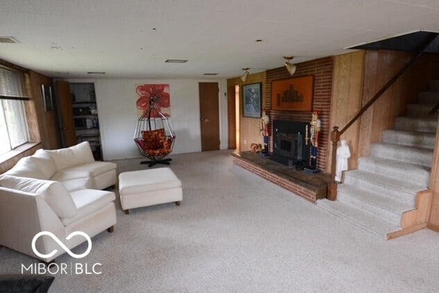 carpeted living room featuring wood walls, visible vents, a fireplace, and stairs