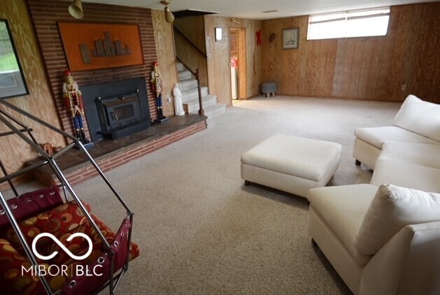 carpeted living room featuring wooden walls and stairs