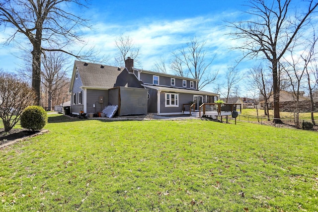 back of property with a lawn, a chimney, fence, and a wooden deck