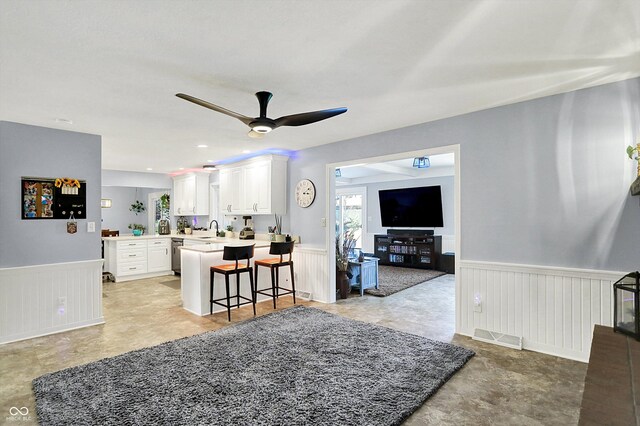 6820 W Forest Brook Dr, Fountaintown, IN 46130 - kitchen featuring wainscoting, a sink, ceiling fan, a peninsula, and a kitchen breakfast bar