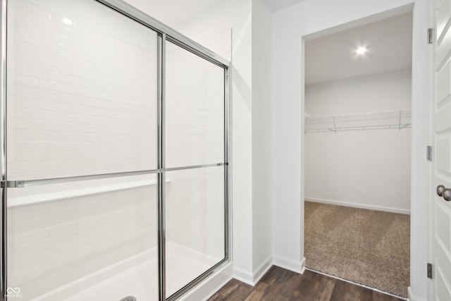 full bath featuring baseboards, wood finished floors, a spacious closet, and a shower stall