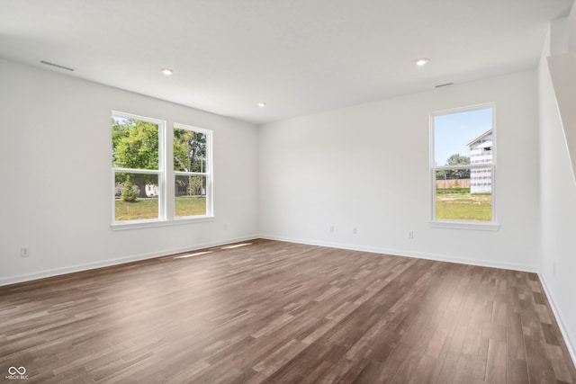 unfurnished room featuring baseboards, visible vents, dark wood-type flooring, and a healthy amount of sunlight