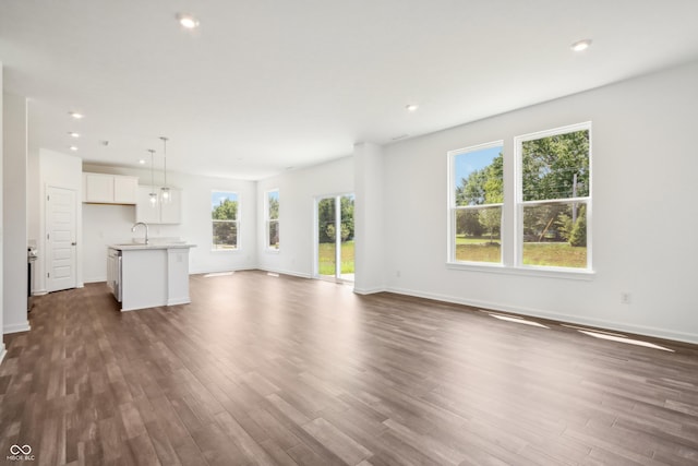 unfurnished living room featuring baseboards, recessed lighting, dark wood-type flooring, and a sink