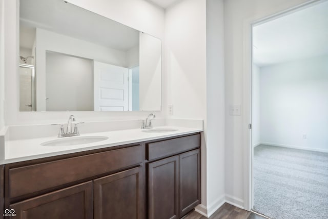full bathroom with double vanity, an enclosed shower, baseboards, and a sink