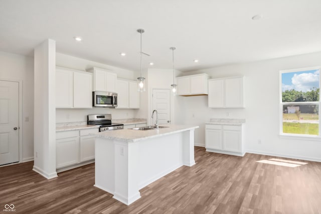 kitchen with wood finished floors, appliances with stainless steel finishes, white cabinetry, an island with sink, and a sink
