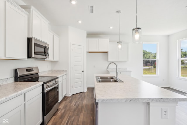 kitchen featuring light countertops, stainless steel appliances, dark wood-type flooring, a sink, and a kitchen island with sink