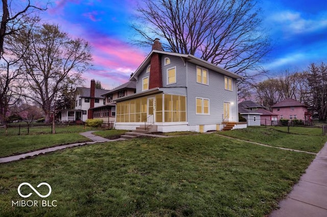 property exterior at dusk featuring a chimney, a sunroom, fence, entry steps, and a lawn