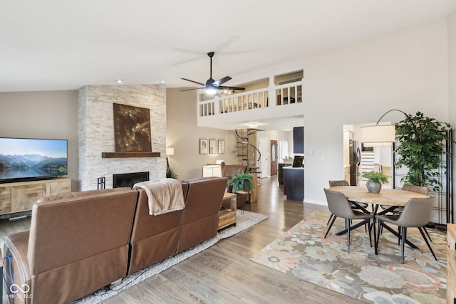 living area featuring a fireplace, a towering ceiling, a ceiling fan, wood finished floors, and baseboards