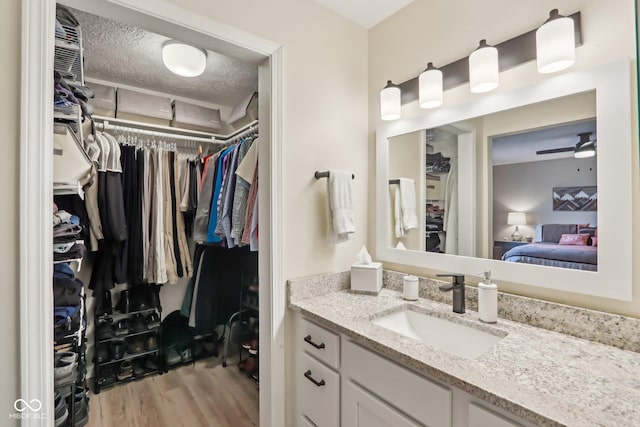bathroom featuring a spacious closet, a textured ceiling, connected bathroom, vanity, and wood finished floors