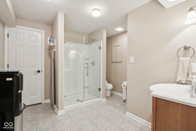 bathroom with a textured ceiling, vanity, toilet, a stall shower, and baseboards