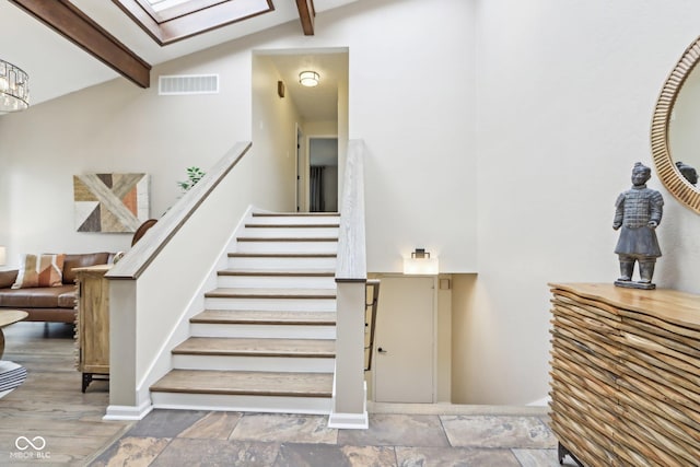 staircase with high vaulted ceiling, visible vents, a skylight, baseboards, and beam ceiling
