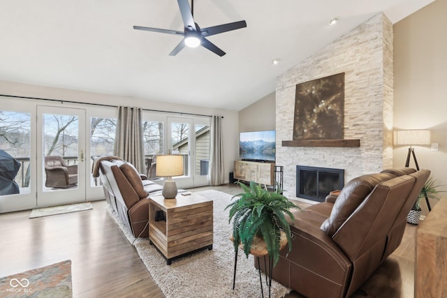 living room with wood finished floors, high vaulted ceiling, a ceiling fan, and a stone fireplace