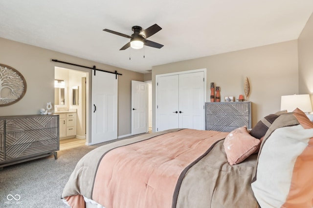 carpeted bedroom with a barn door, a closet, connected bathroom, and ceiling fan