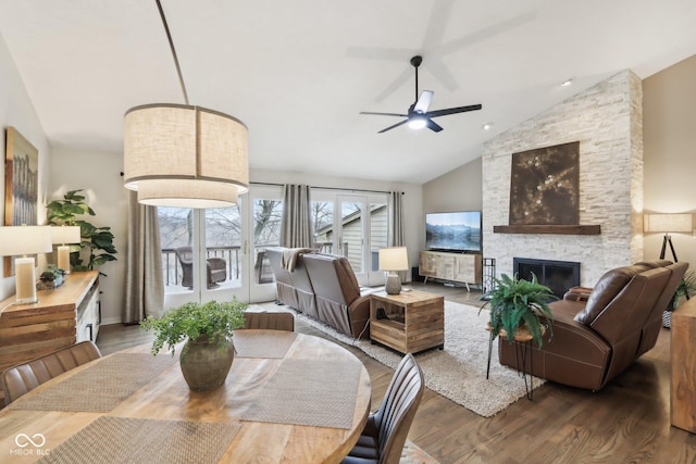 dining space featuring a stone fireplace, a ceiling fan, wood finished floors, and lofted ceiling