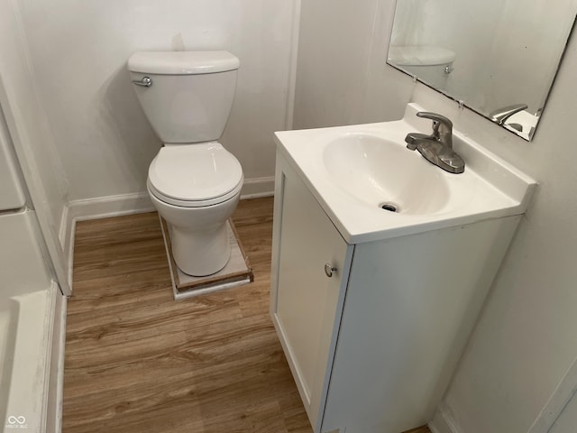 half bathroom featuring toilet, wood finished floors, baseboards, and vanity