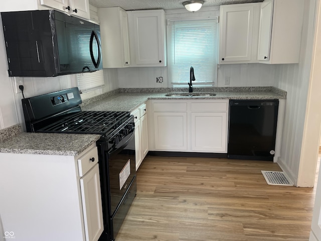 kitchen with a sink, visible vents, white cabinets, and black appliances