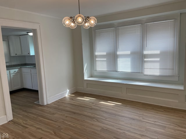 unfurnished dining area featuring baseboards, dark wood-style floors, an inviting chandelier, and ornamental molding