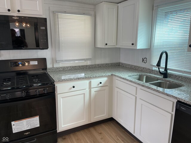 kitchen with light stone counters, a sink, white cabinets, wood finished floors, and black appliances