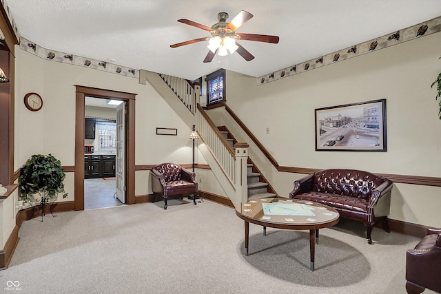 living area with a ceiling fan, carpet floors, baseboards, and stairway