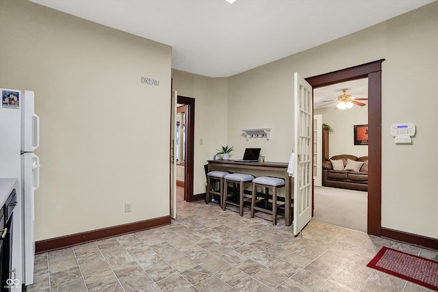 interior space with baseboards, a ceiling fan, and freestanding refrigerator