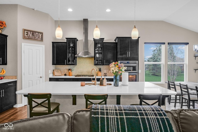 kitchen with wall chimney range hood, light countertops, a kitchen bar, dark cabinetry, and stainless steel appliances