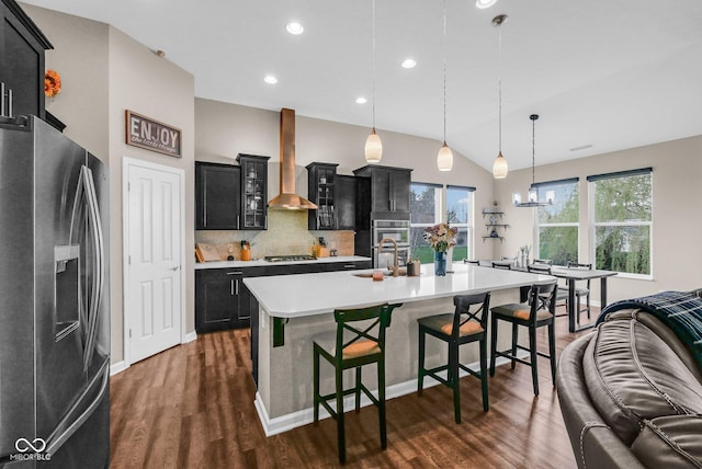 kitchen with wall chimney range hood, light countertops, a kitchen bar, dark cabinetry, and appliances with stainless steel finishes
