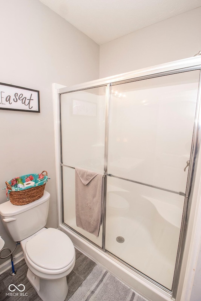 full bath with a shower stall, wood finished floors, and toilet