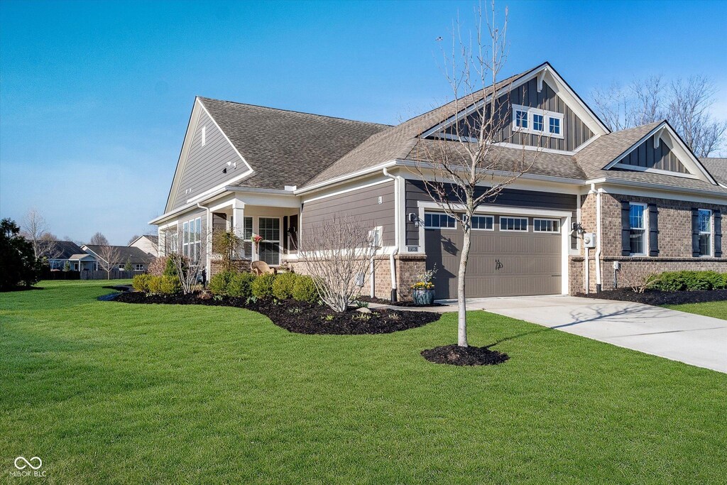 craftsman house with driveway, an attached garage, board and batten siding, brick siding, and a front lawn