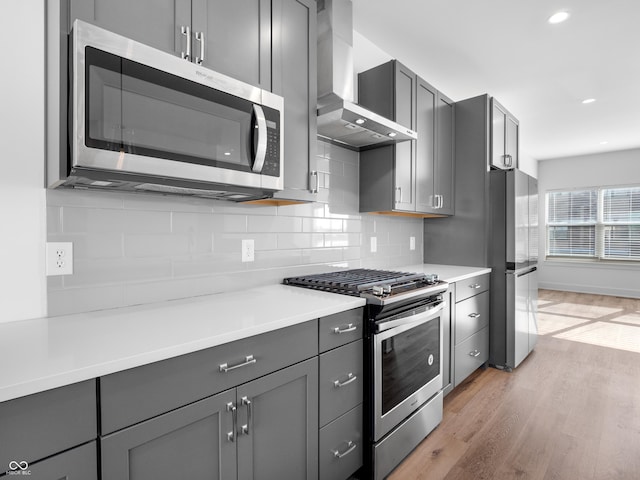 2578 Filson St, Carmel, IN 46032 - kitchen with wall chimney range hood, decorative backsplash, gray cabinets, light wood-style floors, and stainless steel appliances