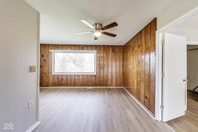 7906 E 21st St, Indianapolis, IN 46219 - spare room with light wood-type flooring, wood walls, baseboards, and ceiling fan
