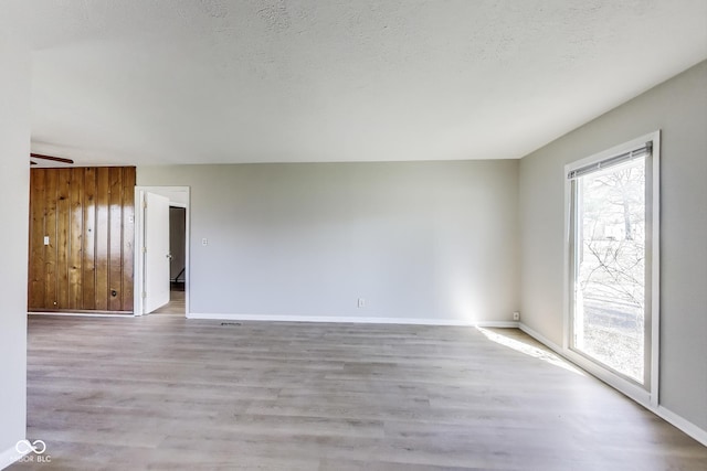 7906 E 21st St, Indianapolis, IN 46219 - unfurnished room featuring wood walls, a textured ceiling, baseboards, and wood finished floors