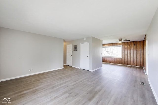 7906 E 21st St, Indianapolis, IN 46219 - unfurnished living room featuring wood walls, baseboards, visible vents, a ceiling fan, and wood finished floors
