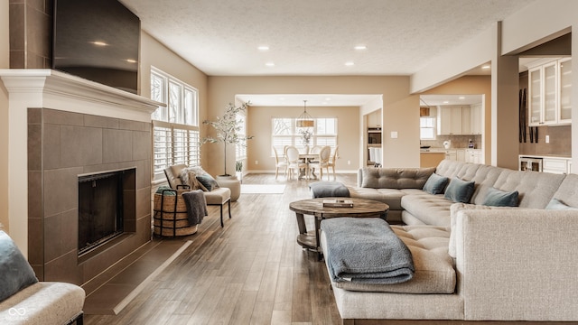 living area featuring a textured ceiling, a tile fireplace, baseboards, wood finished floors, and recessed lighting