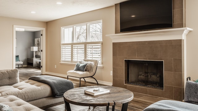 living area with baseboards, recessed lighting, wood finished floors, and a tiled fireplace