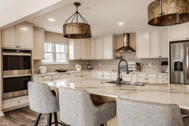 kitchen with a sink, stainless steel appliances, wall chimney range hood, decorative backsplash, and dark wood-style flooring